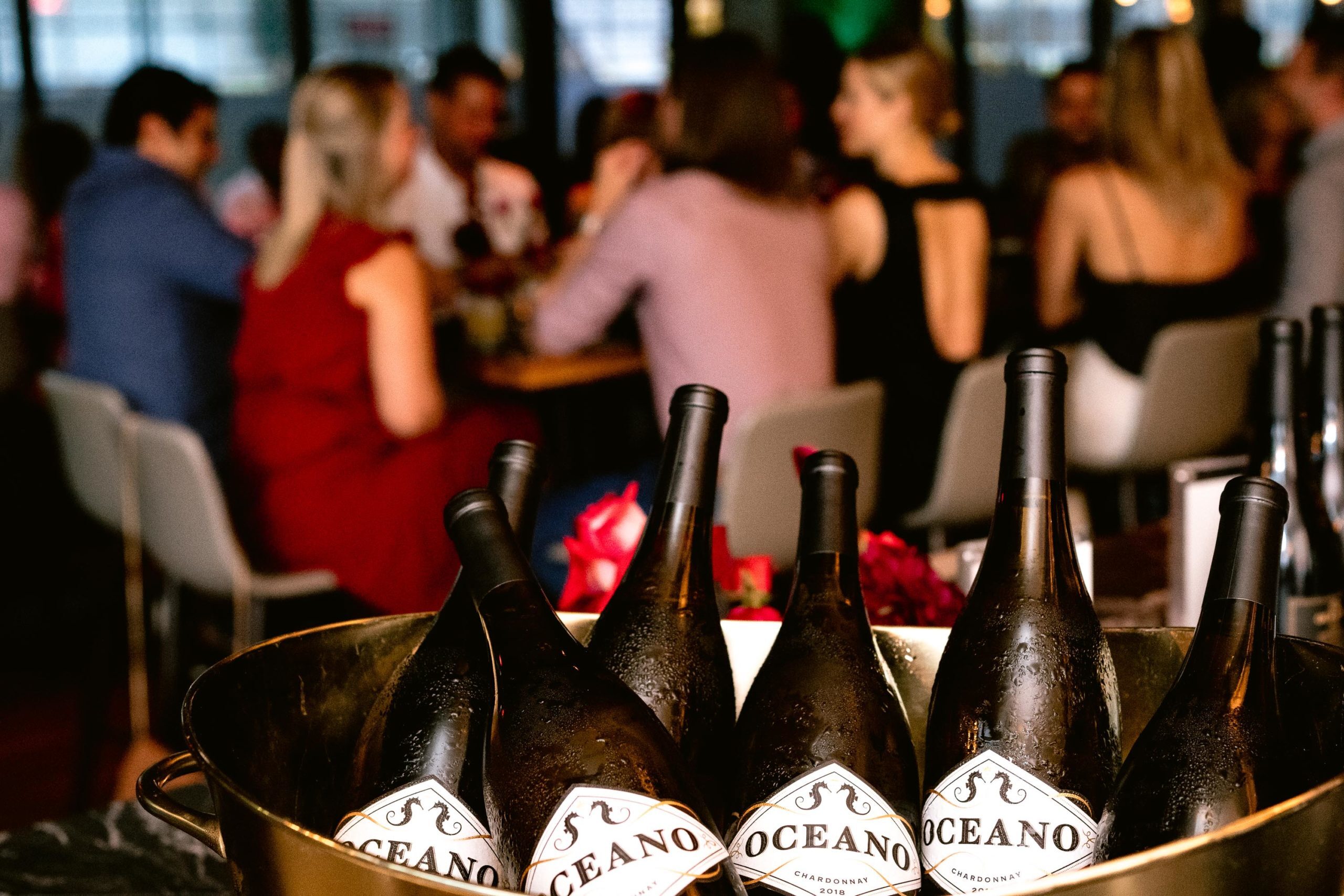 bucket of Oceano wine bottles with dinner party in background