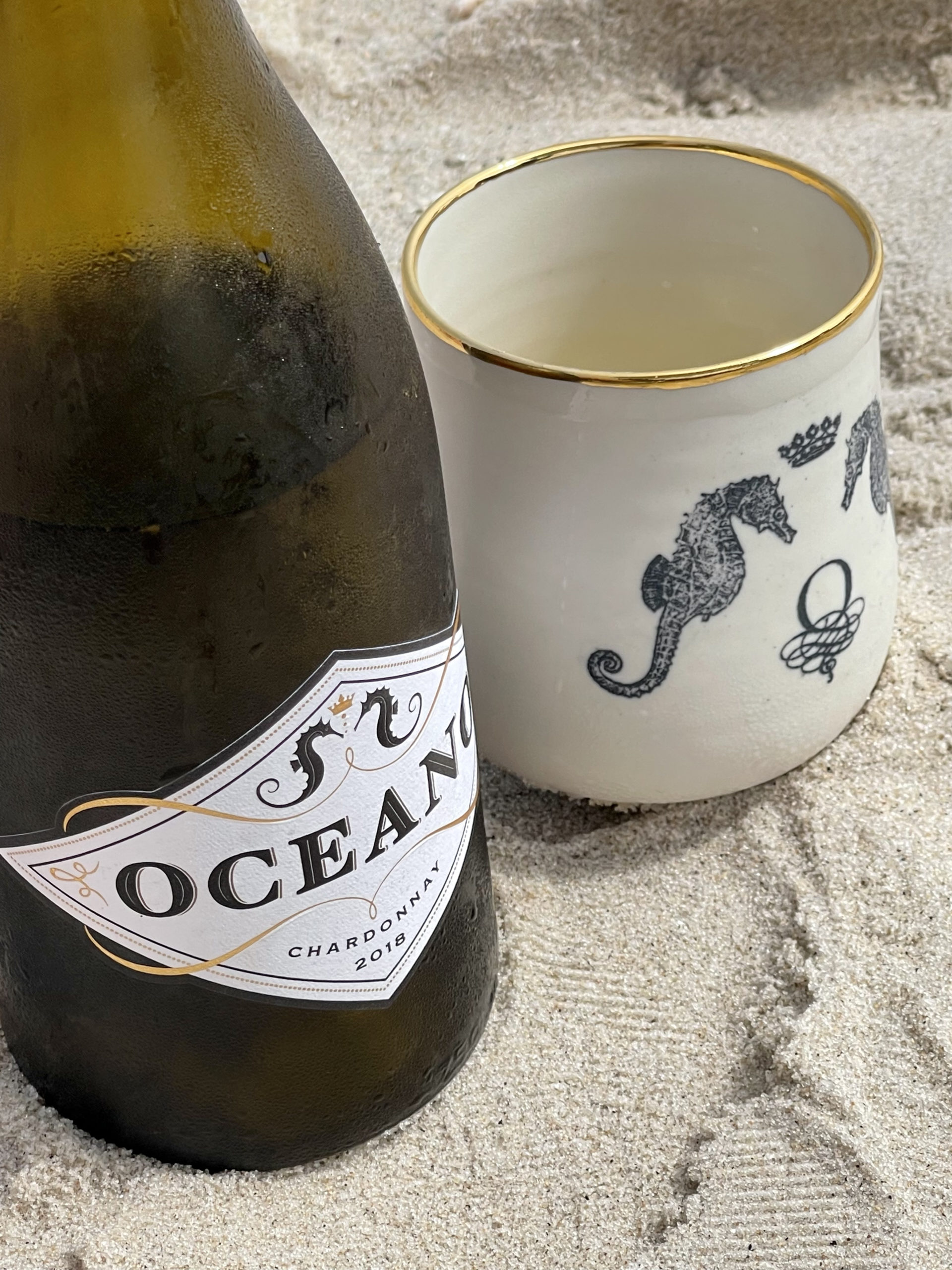 Oceano Wine Chardonnay bottle and Oceano Wine goblet placed on sand