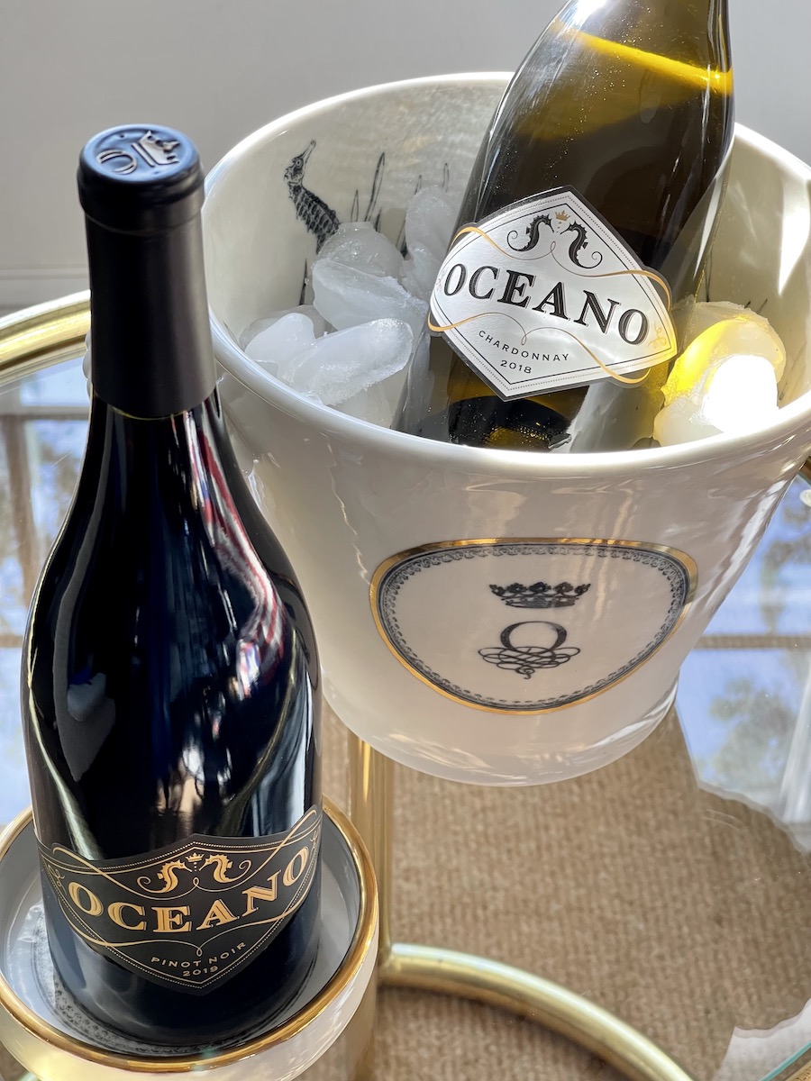 Bottle of Oceano Chardonnay chilling in custom Oceano ice bucket and bottle of Oceano Pinot Noir sitting atop a custom Oceano bottle coaster.