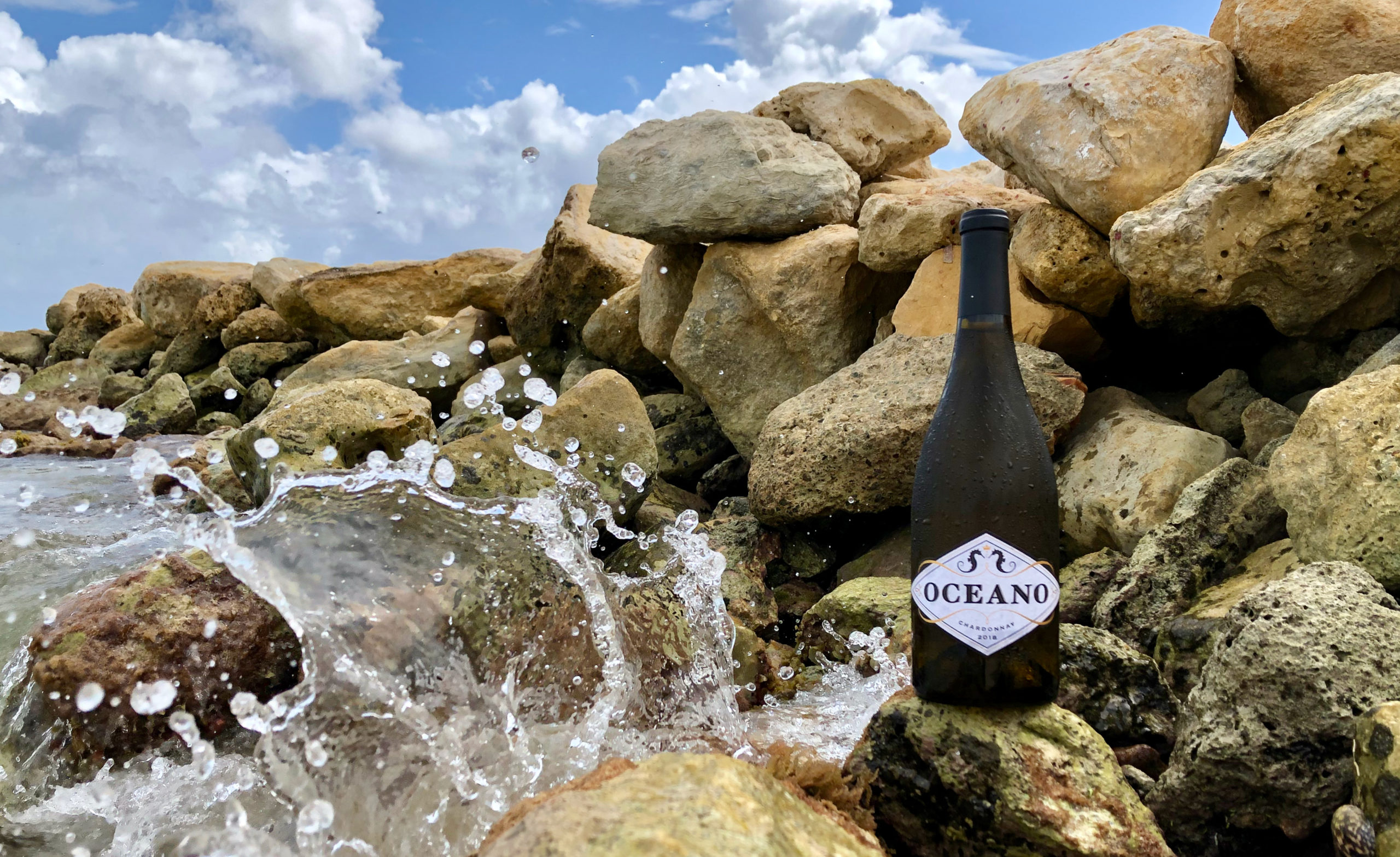 water splashing on rocks with an Oceano wine bottle on one