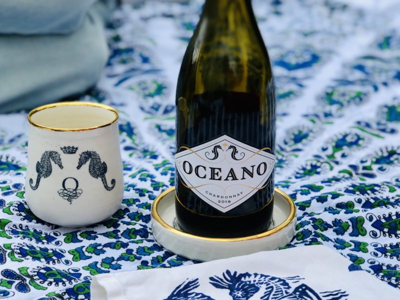 Oceano wine goblet and bottle coaster pictured on blue blanket with bottle of Oceano Chardonnay wine.