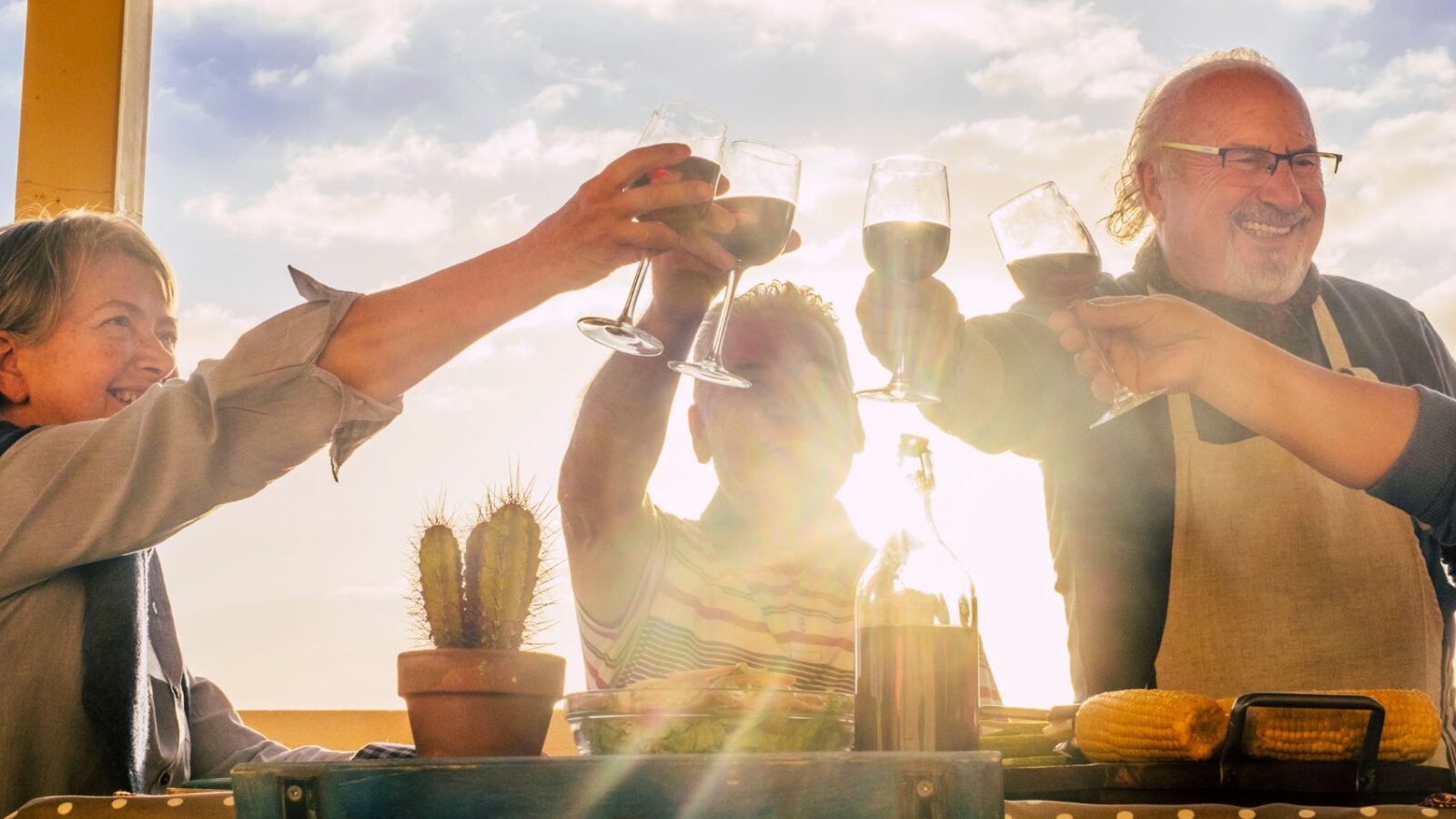 Four people toasting with wine glasses in a desert location with the sun shining on them.