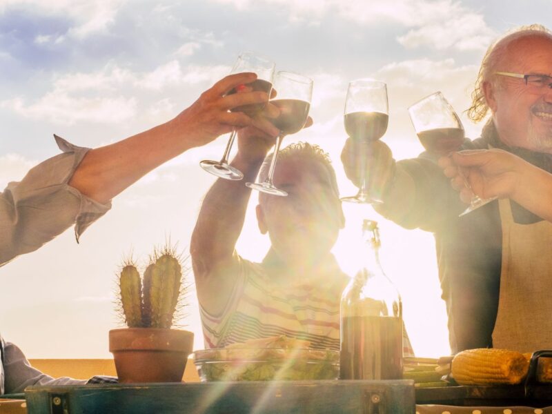 Four people toasting with wine glasses in a desert location with the sun shining on them.