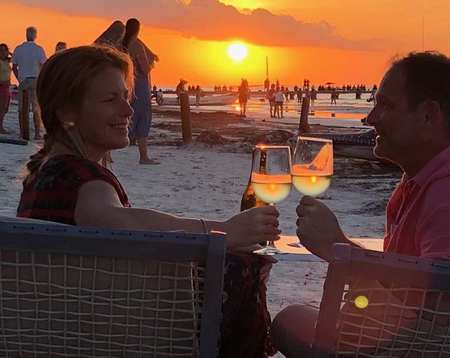 A couple sharing wine on the beach with the sun setting in the background