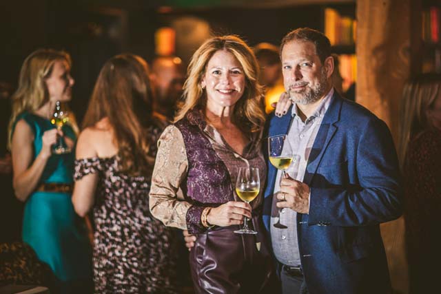 This is the image of our CA wine company's two co-founders, Rachel Martin and Kurt Deutsch. They are dressed up for an event and each holding a glass of white wine (chardonnay wine). The image supports our blog post about what wines to pair with movie watching, particularly movie musical watching.