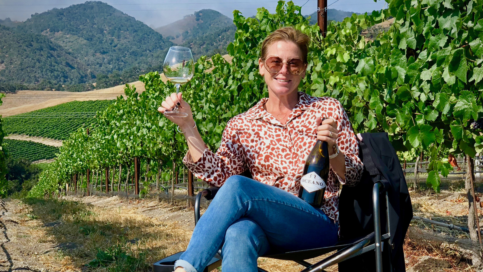 Oceano Wines founder, Rachel Martin sitting in a vineyard and enjoying a glass of Oceano Chardonnay.