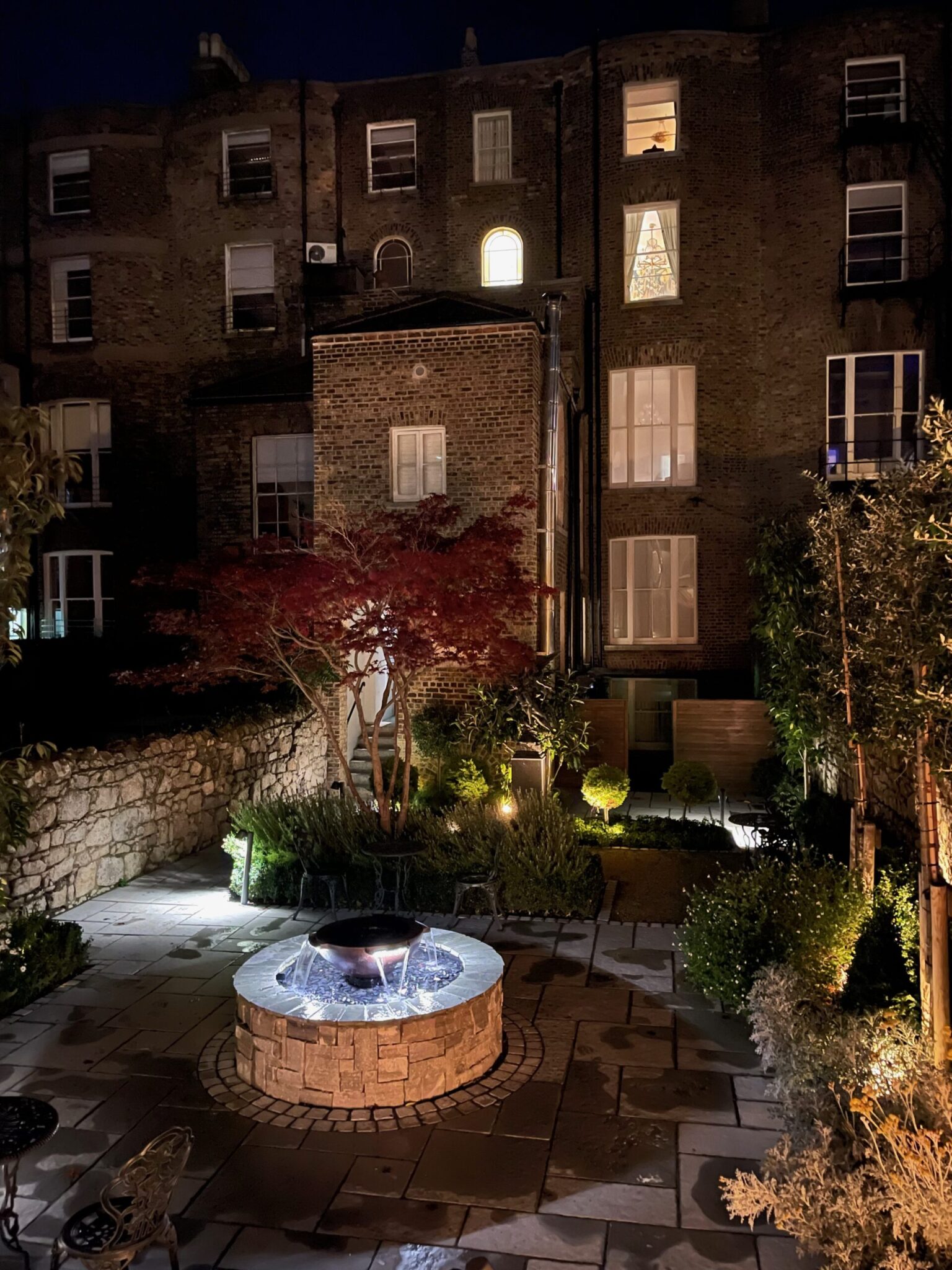 A brick building with a fountain in front of it at night.