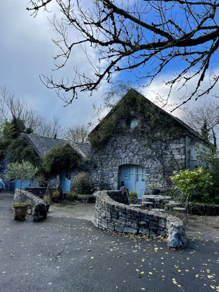 Several trees grow near a stone house with two stone walls leading to it.