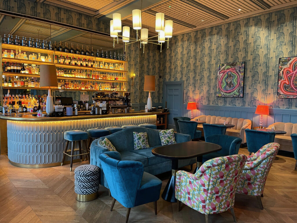 A blue velvet couch and floral chairs next to a bar.