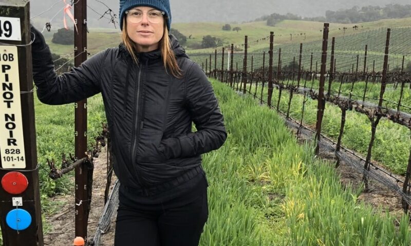 Rachel Martin standing in front of a vineyard of pinot noir grapes.