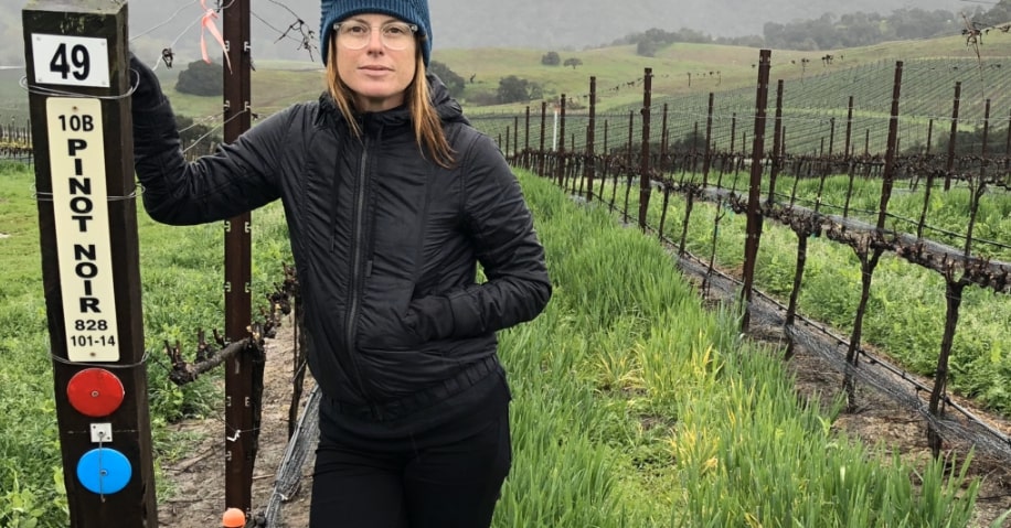 Rachel Martin standing in front of a vineyard of pinot noir grapes.