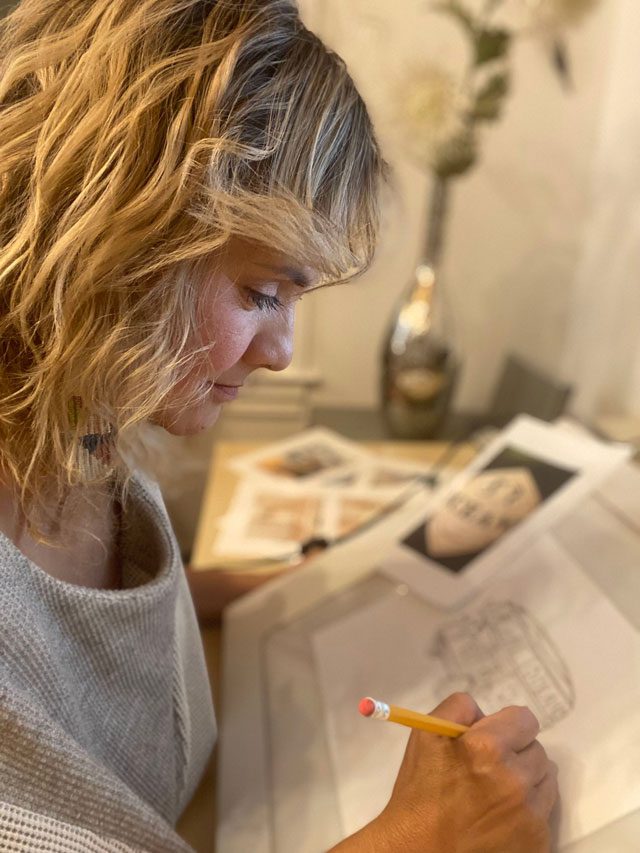 A woman draws a picture of a VW bus with a pencil.