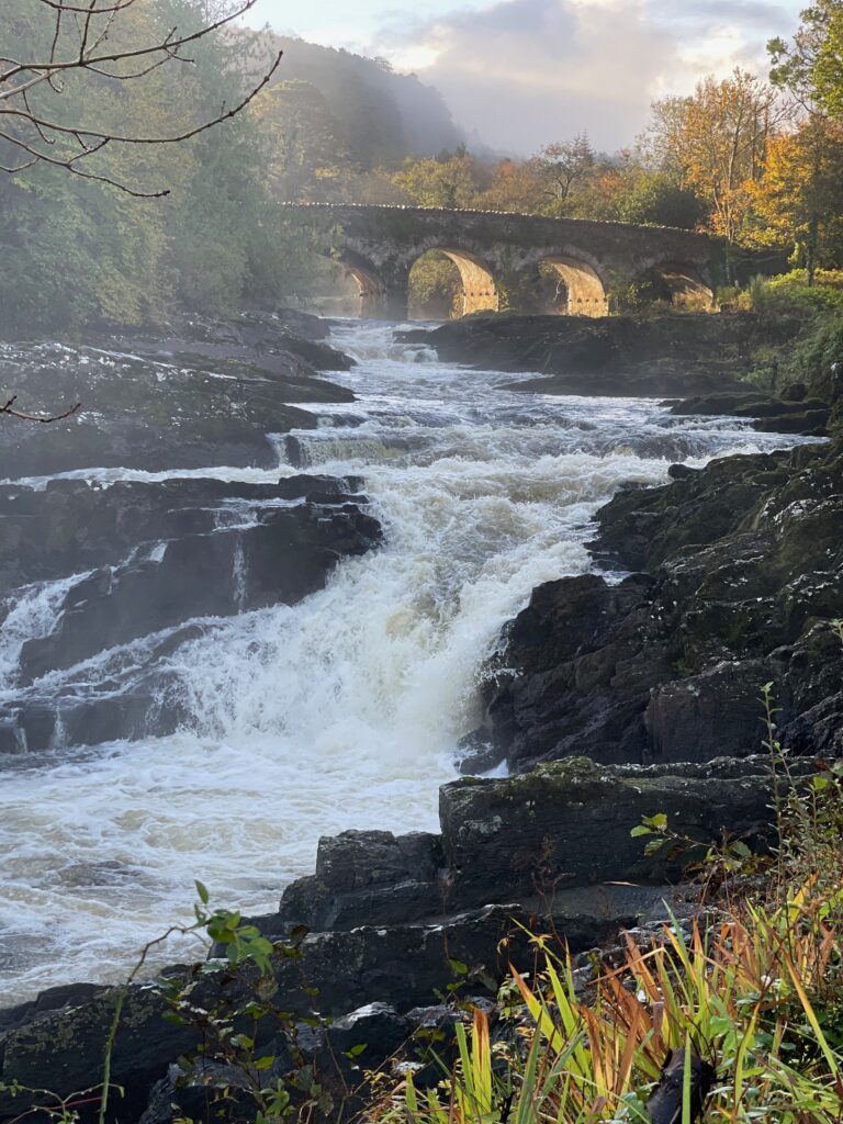 A small water fall in front of a stone bridge.