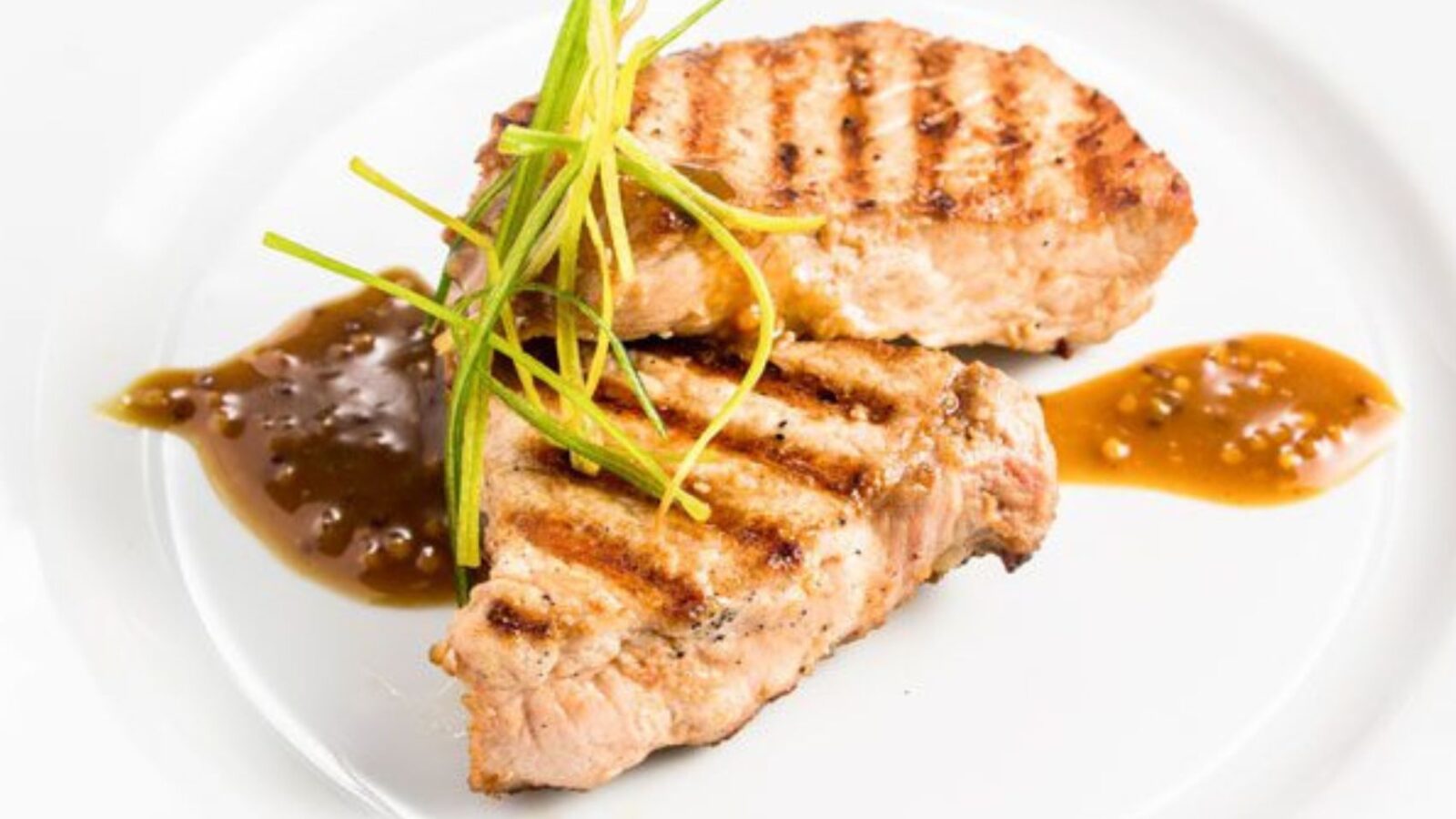 Two garnished pork chops sitting on a white plate.