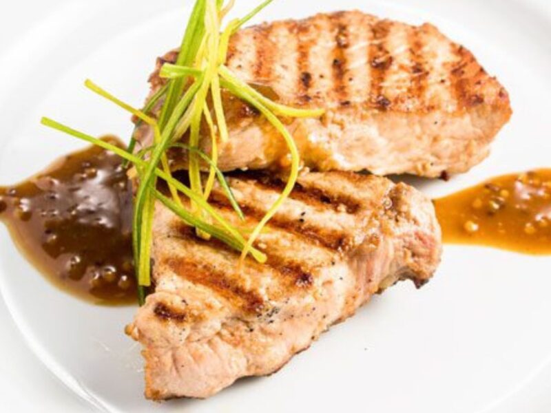 Two garnished pork chops sitting on a white plate.