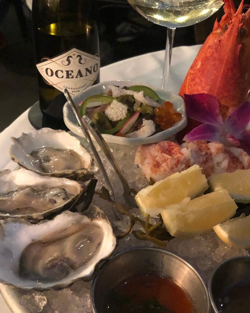 A plate of seafood including lobster and oysters with a bottle of Oceano's Chardonny next to the plate.