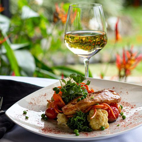 A glass of white wine next to a plate of vegetables and fish, garnished with sprouts.