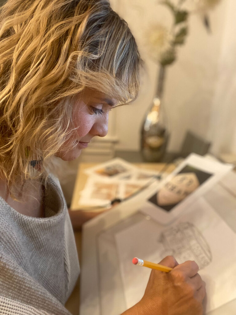 A blonde woman uses a pencil to draw a VW bus.