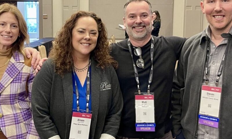 A group of four viticulturalists at a wine convention wearing lanyards and smiling.