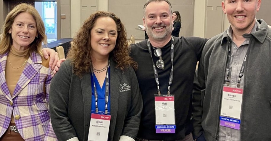 A group of four viticulturalists at a wine convention wearing lanyards and smiling.