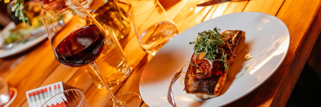 A plate with grilled fish on it topped with greens next to a glass of wine and two glasses of water.