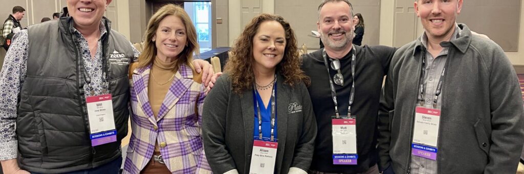 A group of five viticulturalists at a wine convention wearing lanyards and smiling with their arms around each other.