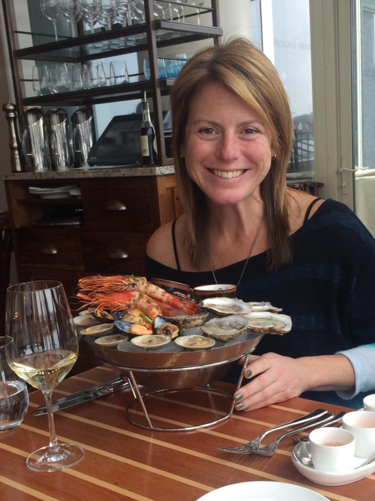 Rachel Martin, owner of Oceano Wines, smiling next to a seafood tower covered in shrimp and oysters.