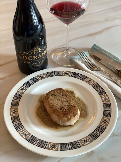 A fine dining experience with a pork chop and Oceano's Pinot Noir wine in a bottle and a glass.