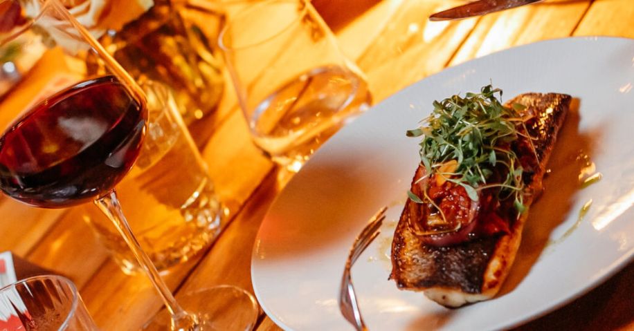 A plate with grilled fish on it topped with greens next to a glass of wine and two glasses of water.