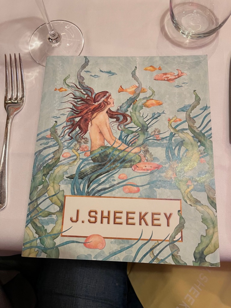 A menu at a seafood restaurant called "J. Sheekey" with an illustration of a mermaid and fish in seaweed on the cover.