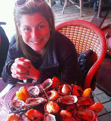 Rachel Martin, founder of Oceano Wines, smiling in front of a platter of seafood at a restaurant.