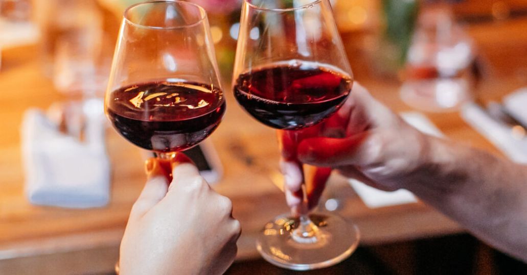 A man and woman holding wine glasses out, about to clink them in a toast.