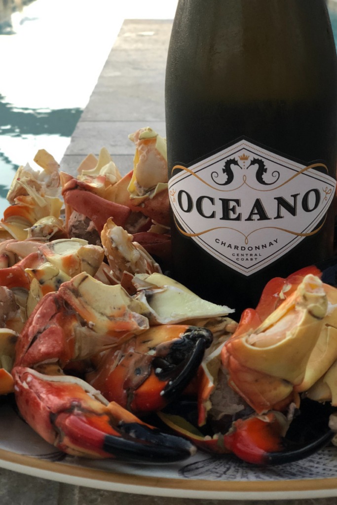 A bottle of Oceano's Chardonnay resting on a table next to a plate full of crab and lobster claws.