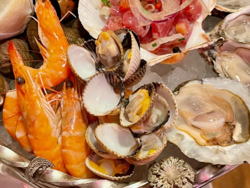 An ornate seafood tower made of a silver metal and topped with shrimp, escargot, and oysters.