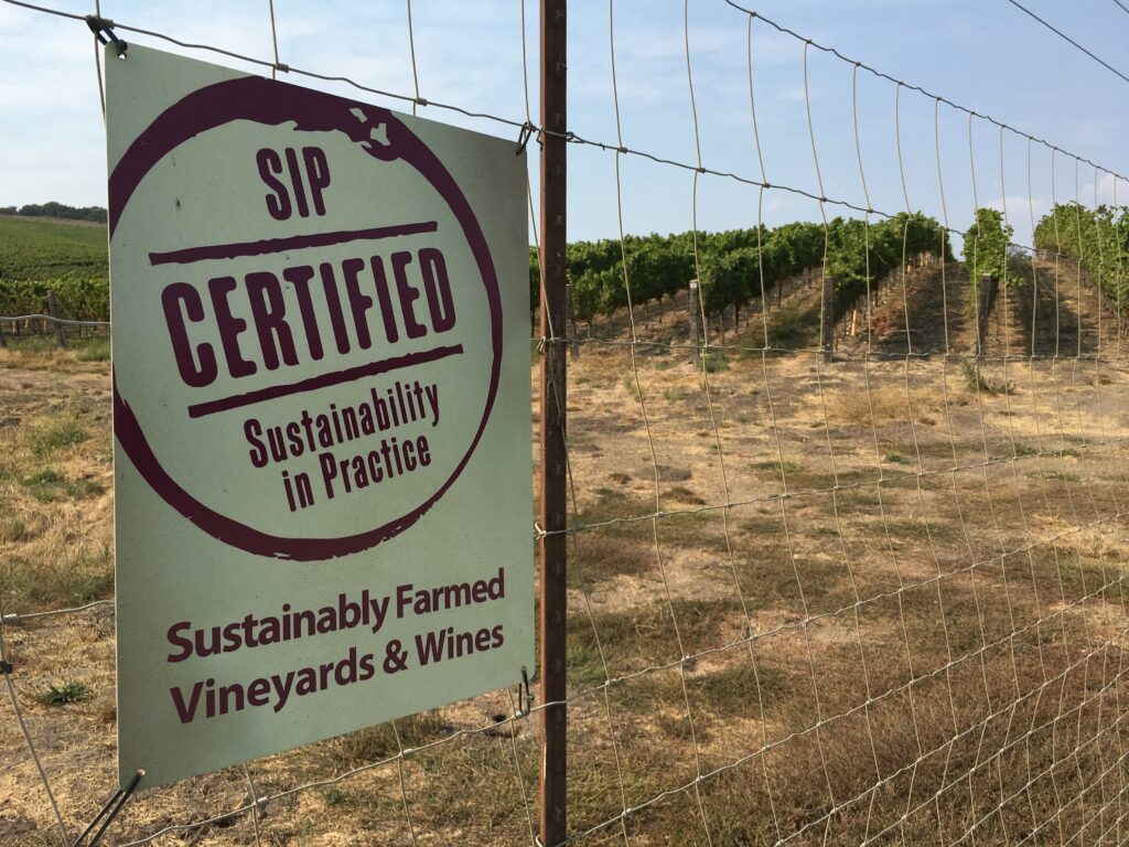 A sign on a fence at Oceano's vineyard that reads "SIP Certified - Sustainability in Practice. Sustainably farmed vineyards & wines."