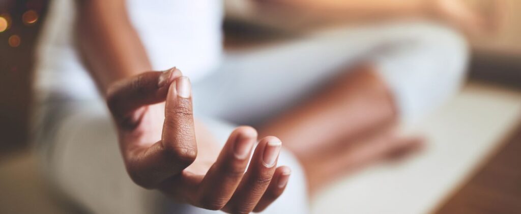 A person with their legs cross presses their thumb and pointer finger together to create an Om hand.