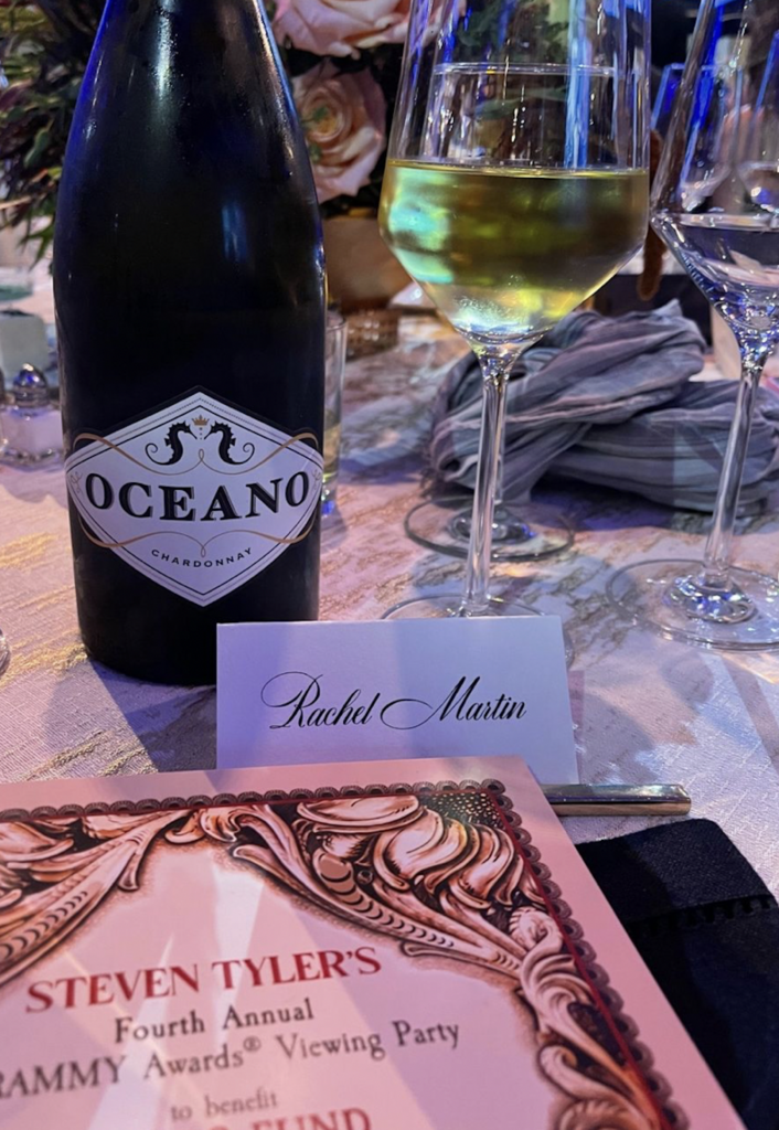 A name card for Rachel Martin at a table with a menu, bottle of wine, and glass of white wine on it.