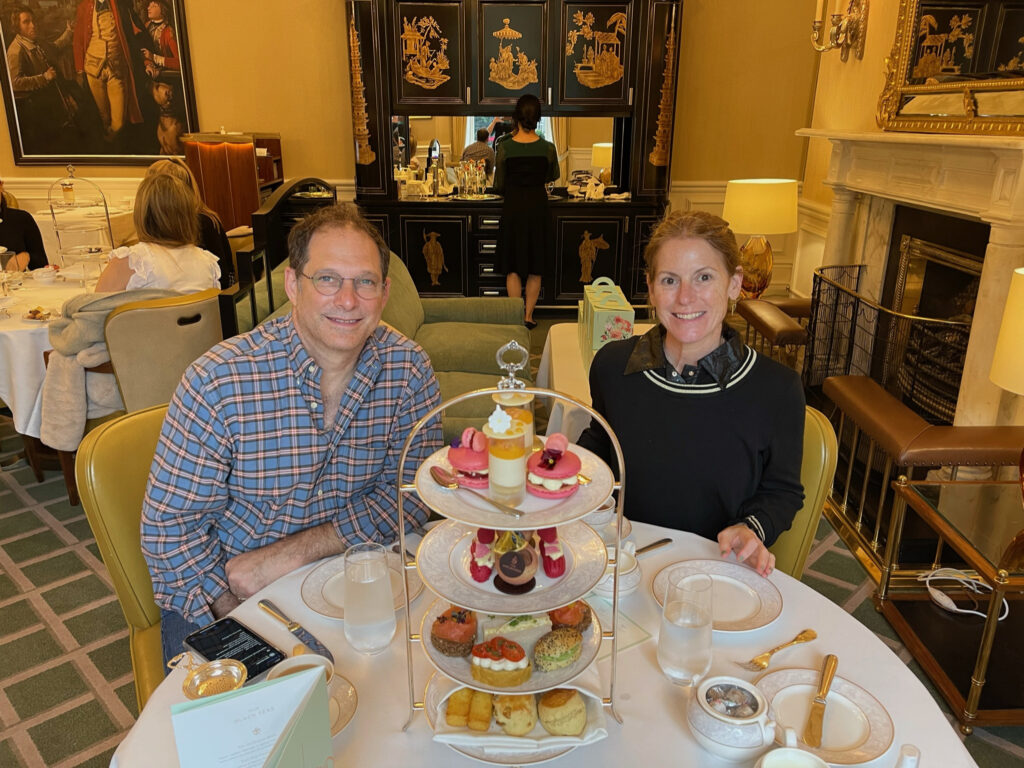 A man and a woman smile while sitting at a white table with different pastries on it.