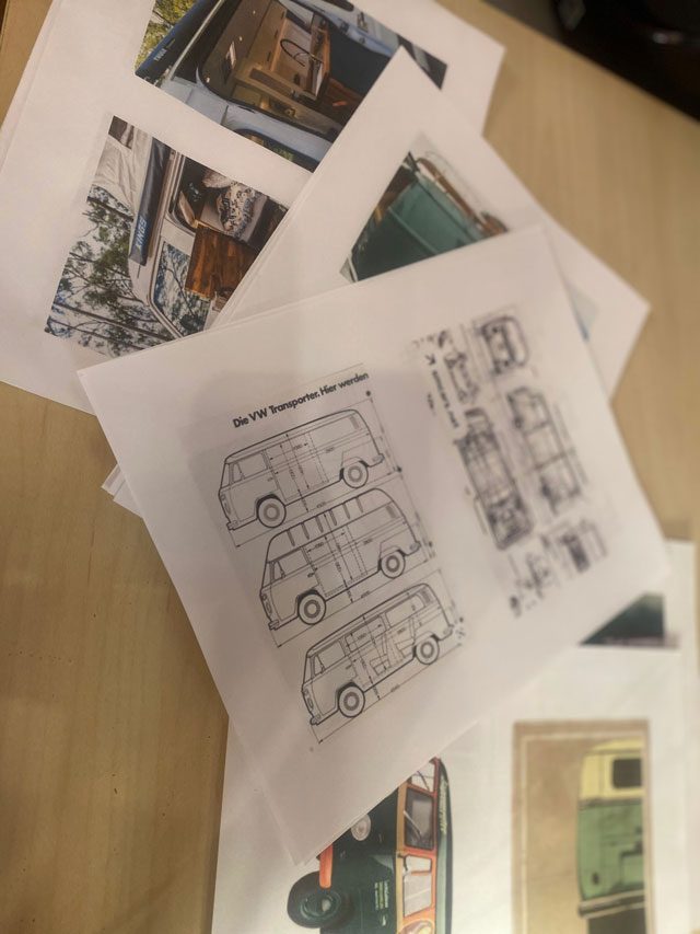 Papers with plans for a VW bus and images of busses on a wood table.