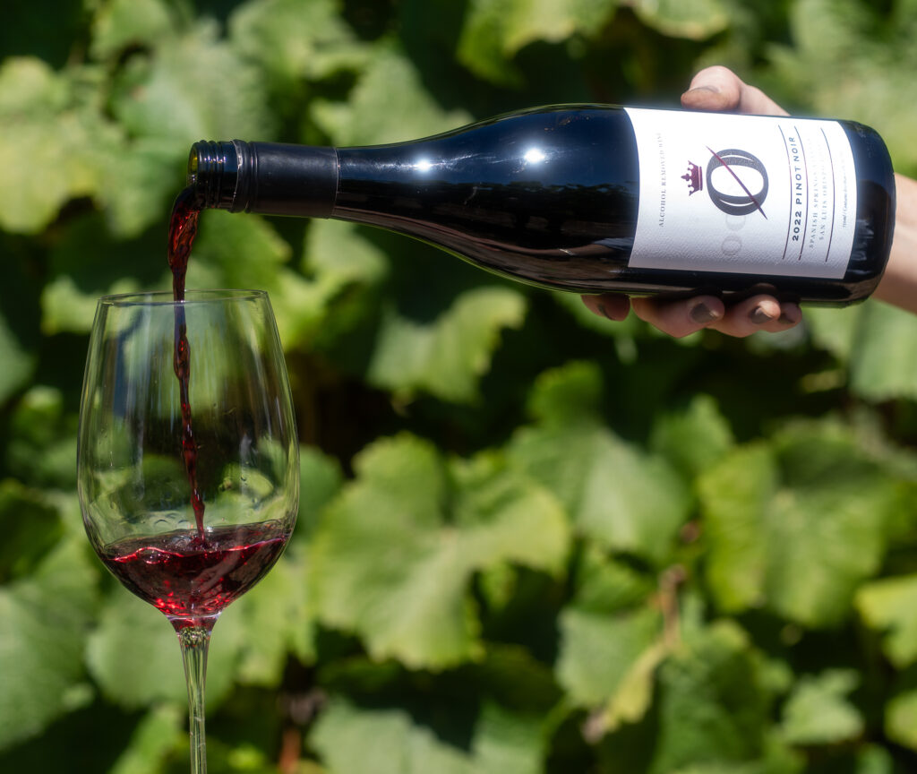 A woman pouring a glass of non-alcoholic Oceano Wine into a wine glass in a vineyard.