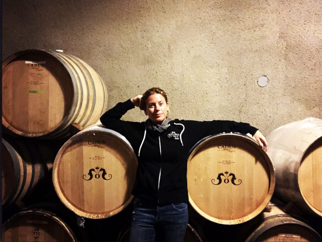 A woman stands between two wine barrels with seahorses on them.