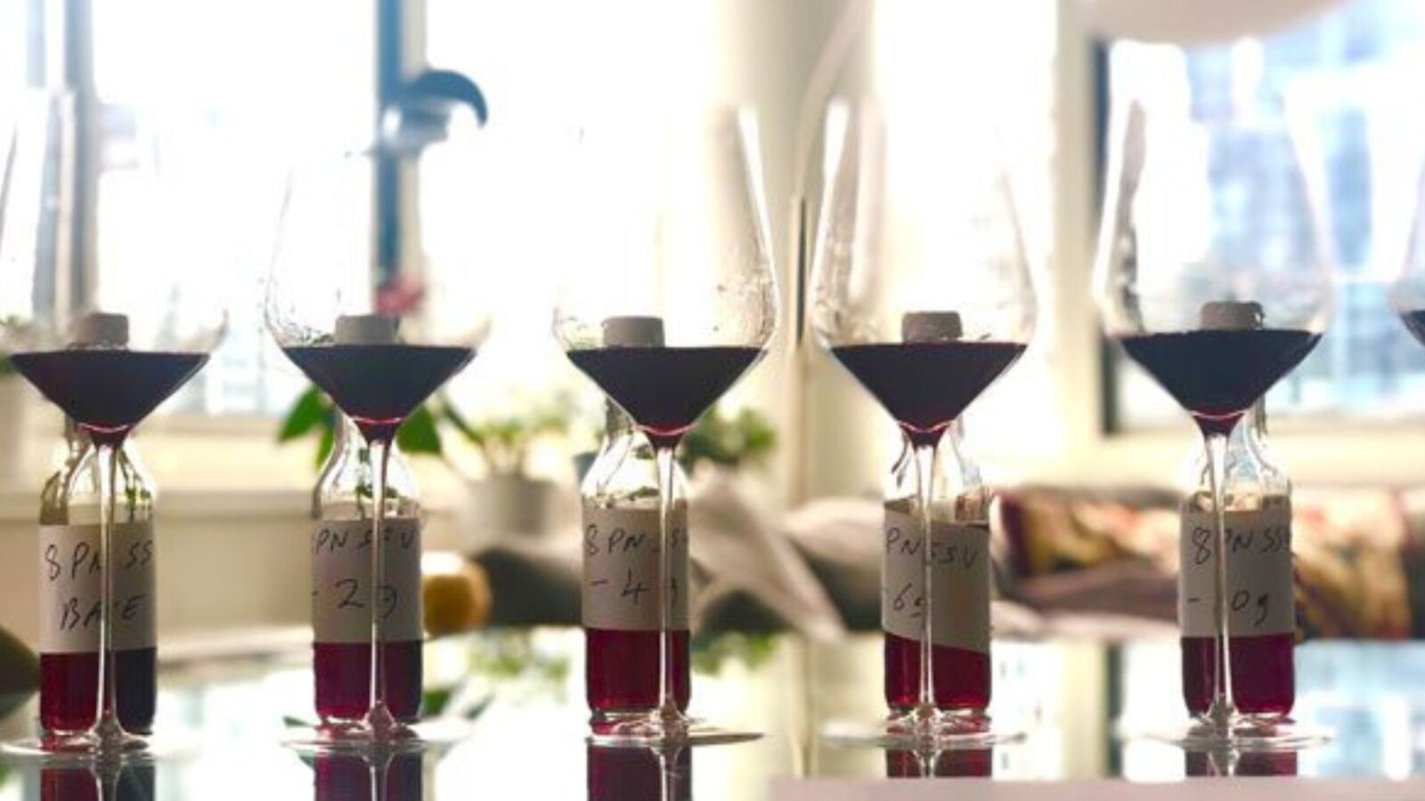 A series of wine glasses with a dash of red wine in each on a glass table.