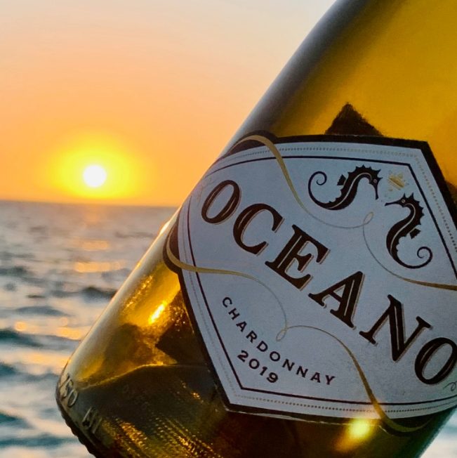 A bottle of Oceano 2019 Chardonnay being held up to the sunset.