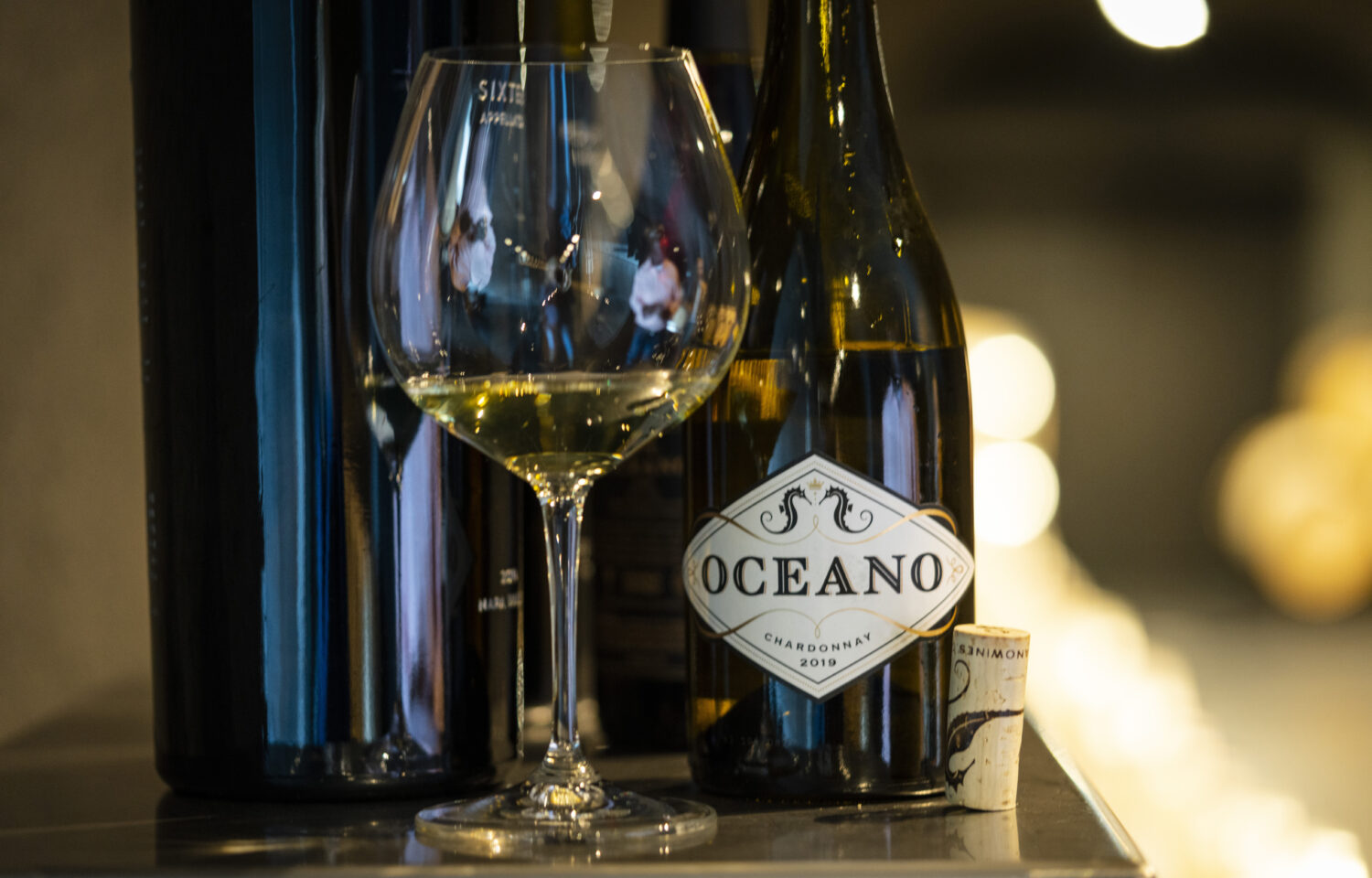 A half poured glass of oceano 2019 chard sitting next to it's corked bottle.