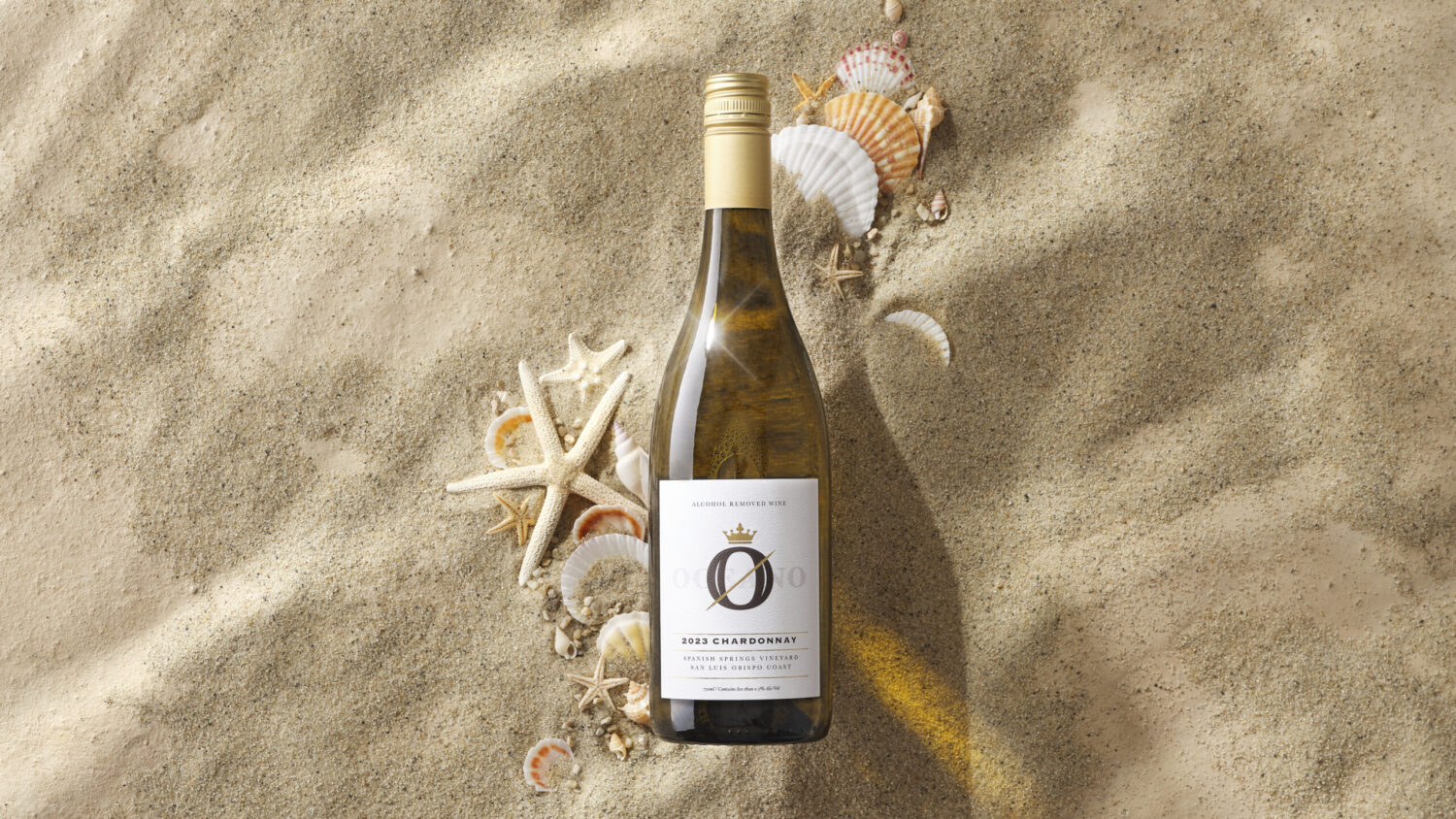 A bottle oceano zero alcohol wine in beach sand surrounded by sea shells.