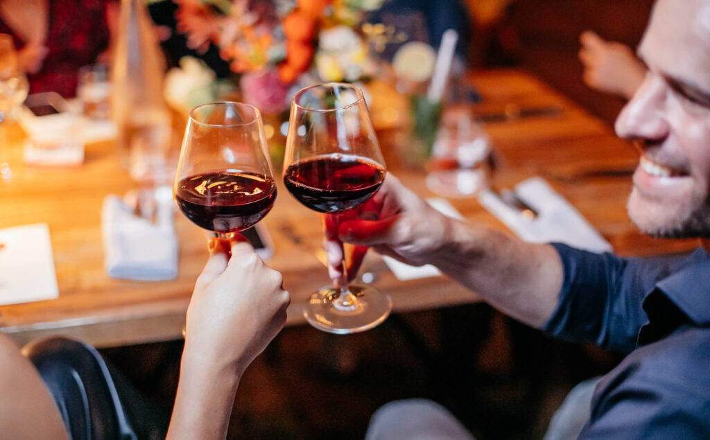 Two people at a wine event toasting glasses with red wine.