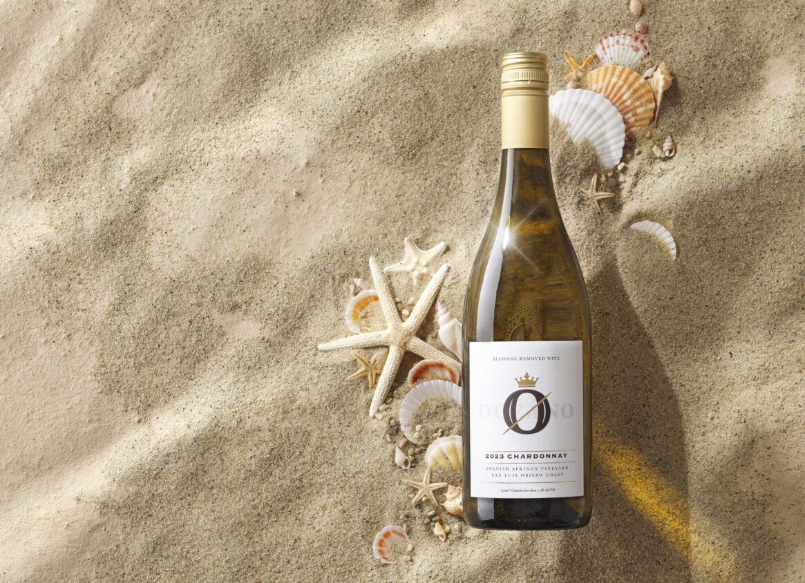 A bottle of oceano zero chard in beach sand.