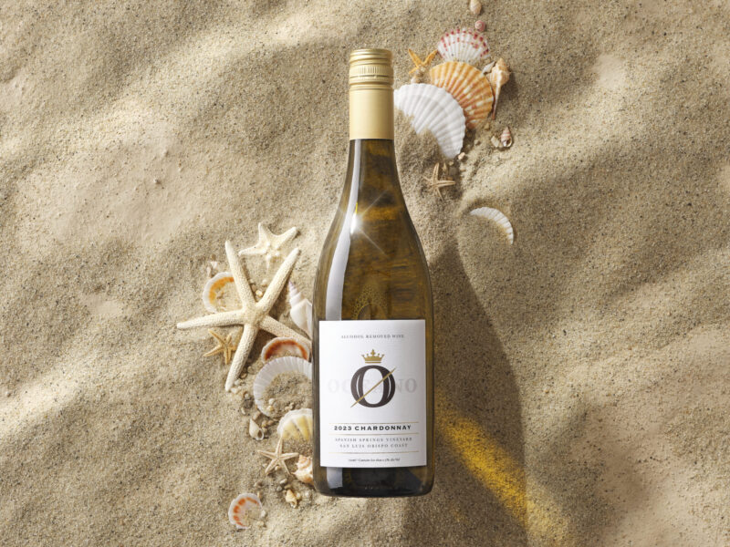 A bottle oceano zero alcohol wine in beach sand surrounded by sea shells.